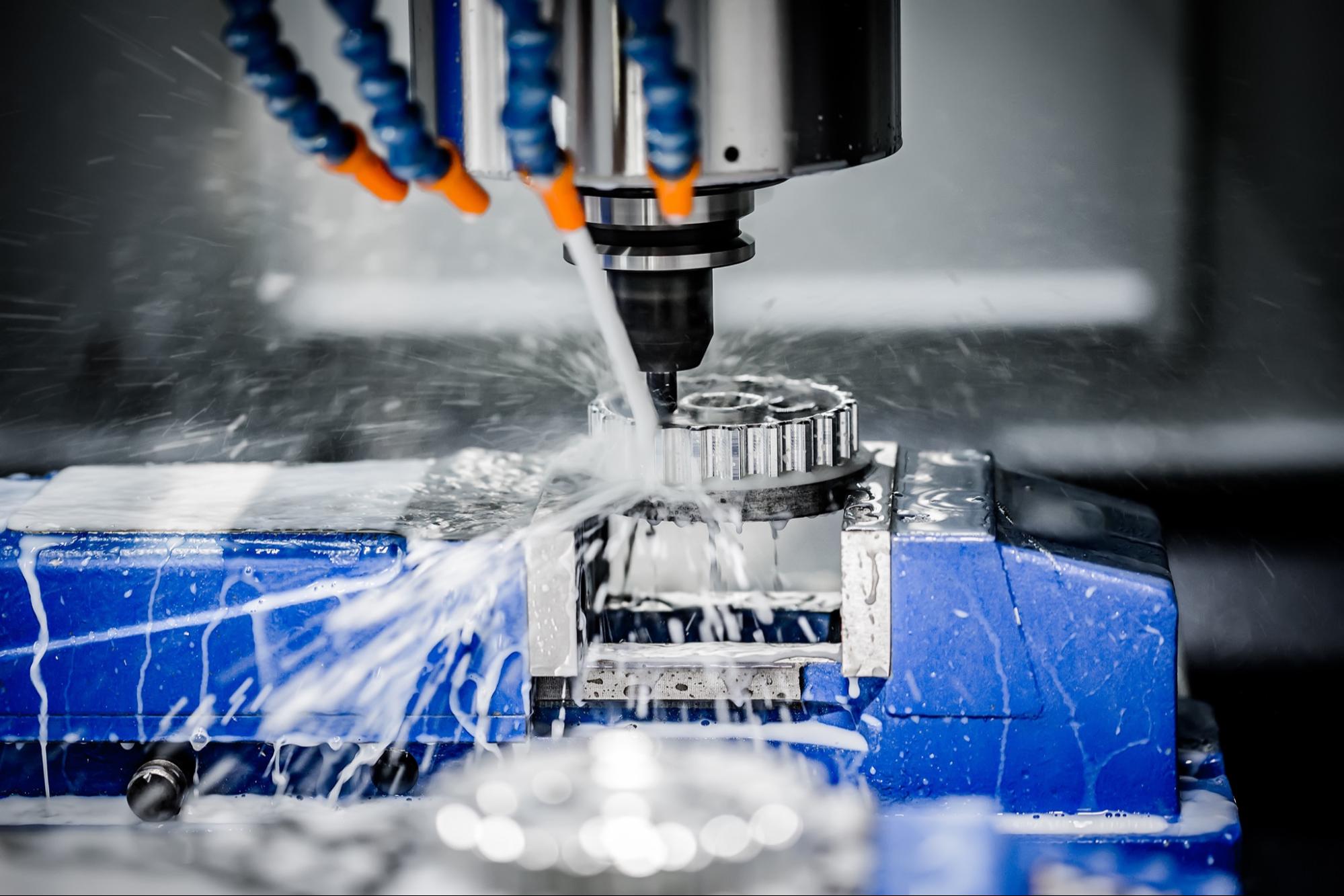 A metal hard being held in a vise in a CNC machine with coolant being sprayed on it