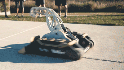 GIF of combat robot deadlift spinning in a circle and picking up a car wheel and tire and buring it with a flamethrower